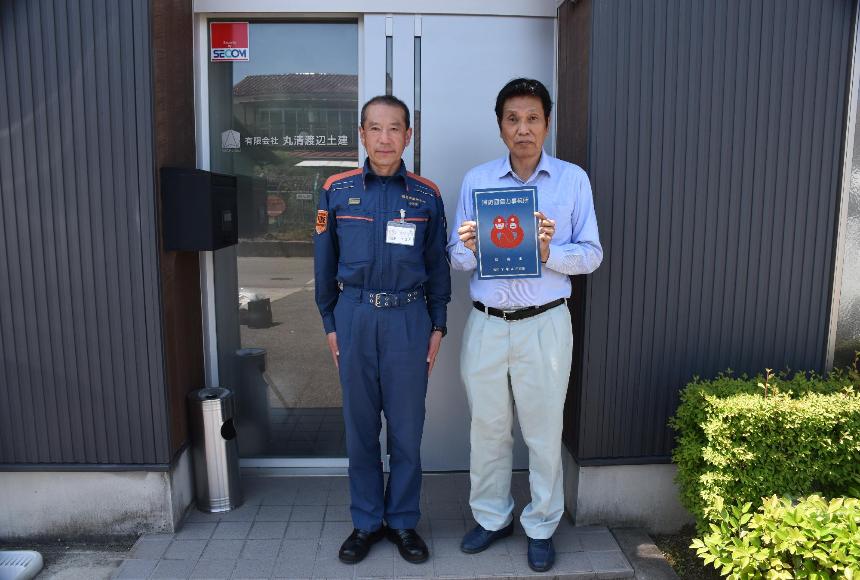 有限会社丸清渡辺土建の建物の前で男性2人が消防団協力事業所表示証を持っている写真